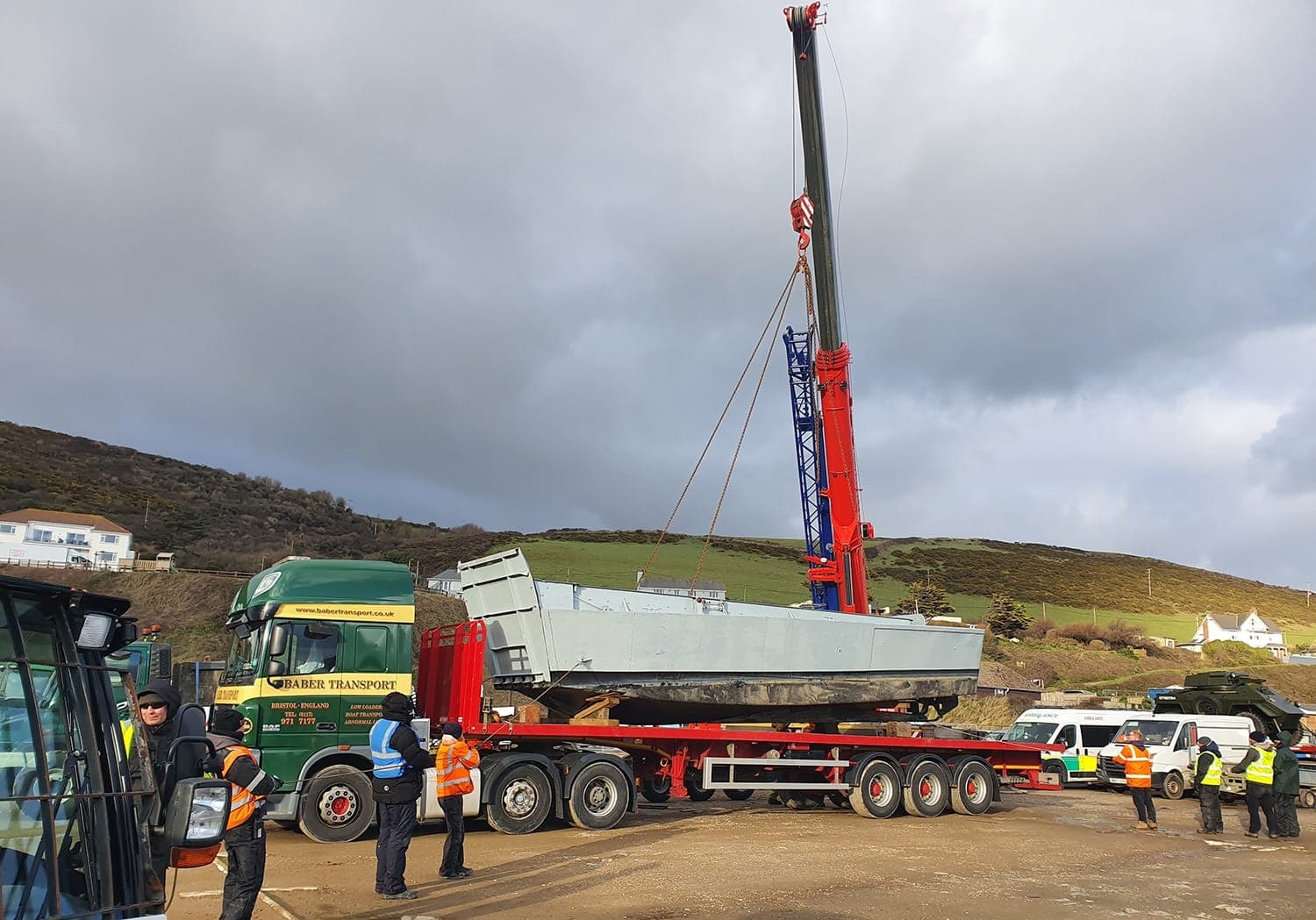 Mobile crane lifting a work boat from a transporter at a coastal location